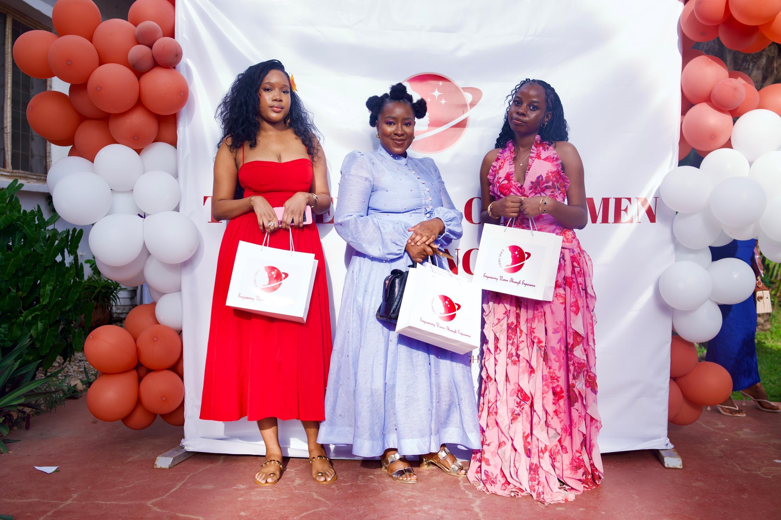 Three women standing in front of a Ladies' Space event backdrop with gift bags